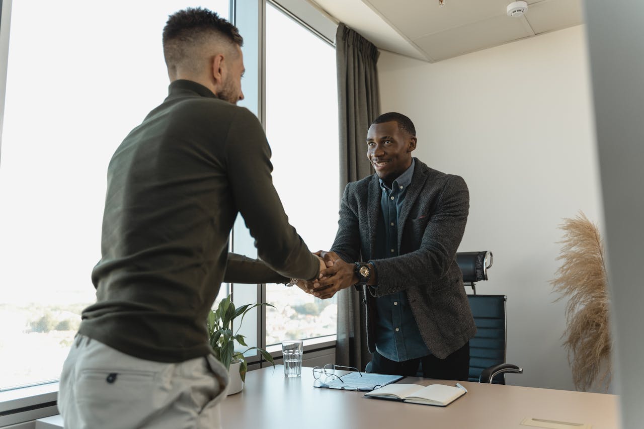 our-story Two businessmen exchanging a handshake during a professional meeting in a modern office setting.